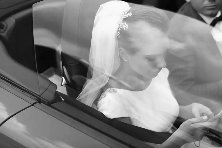 From above black and white of woman in veil text messaging on cellphone near crop anonymous man in automobile on wedding day