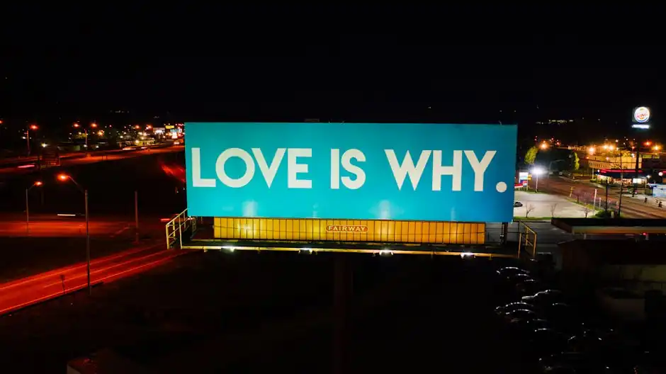 Blue billboard saying Love is why placed on road surrounded by cars and street lights against black night