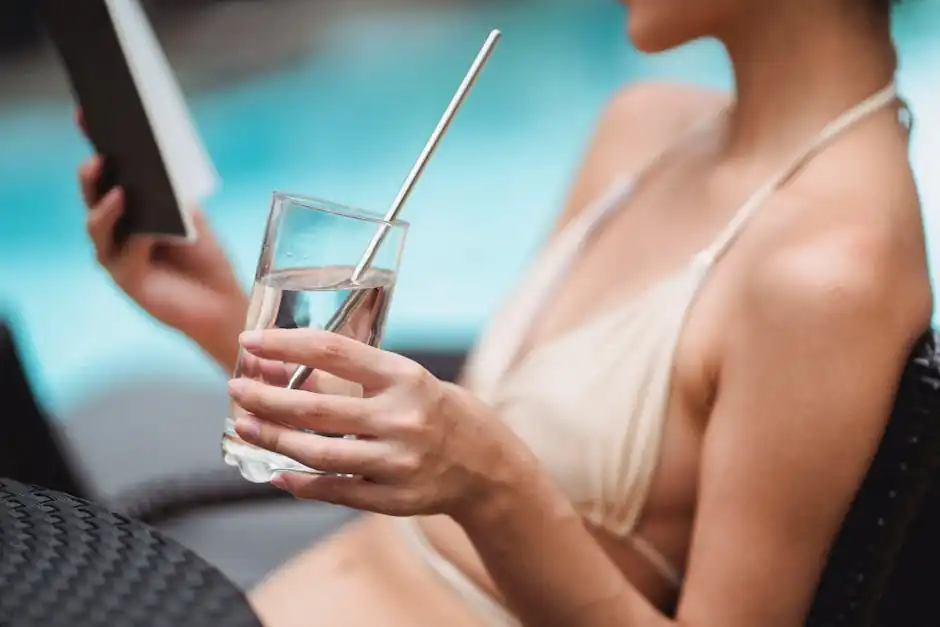 Anonymous woman with glass of water chilling at poolside with book