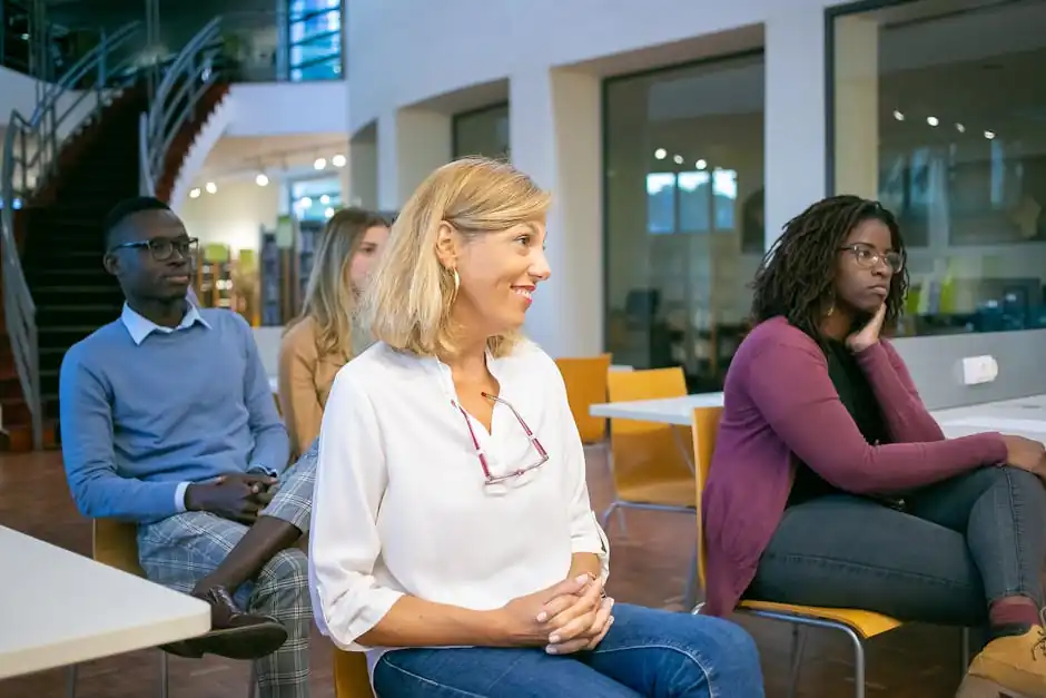 Multiethnic group of students with teacher sitting on chairs in classroom and attentively listening at presentation