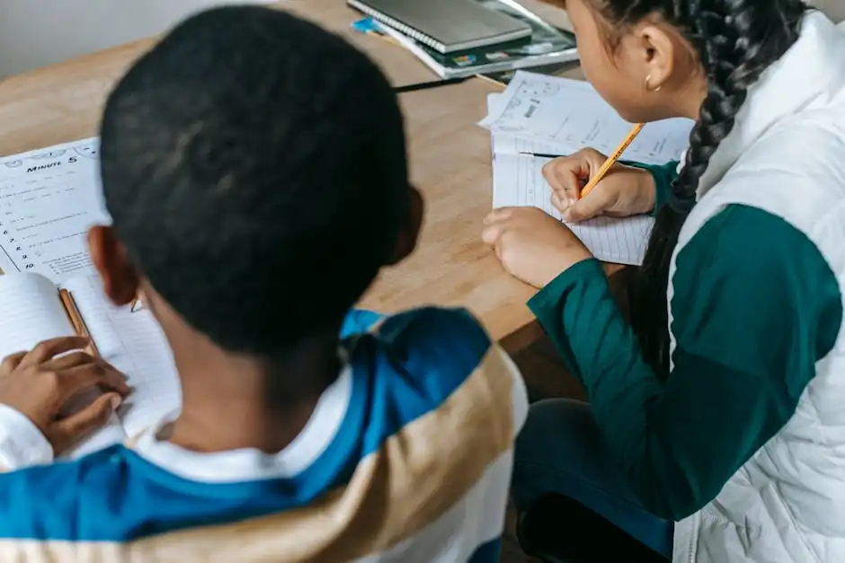 Unrecognizable diverse classmates in casual clothes sitting at school desk and taking notes in copybooks during lesson in classroom