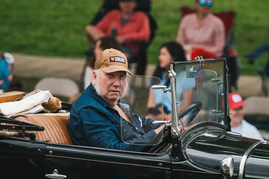 Senior man in a cap driving a vintage car at an outdoor event. Portrays style and nostalgia.