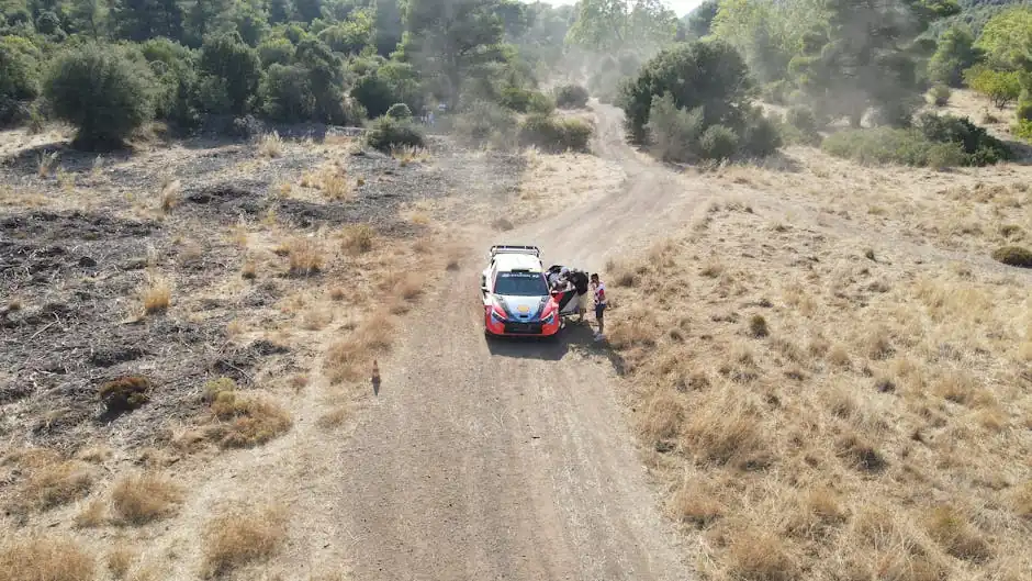 Aerial shot of rally car on a dusty dirt road in Loutraki, Greece, with hills and dry grass.