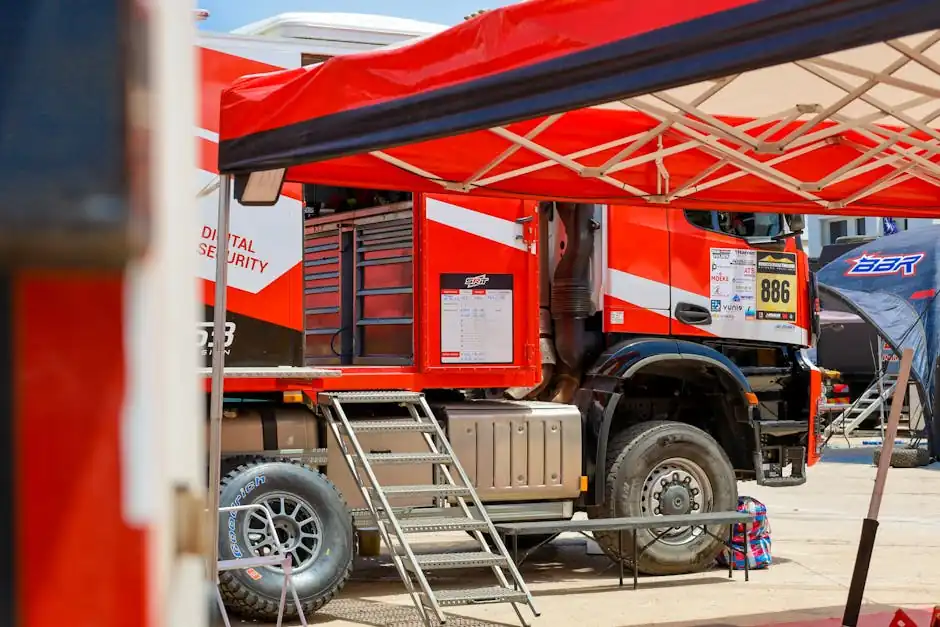 A red rally truck preparing for an outdoor racing event, featuring tents and equipment.